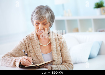 Image of senior female making notes in notepad Stock Photo