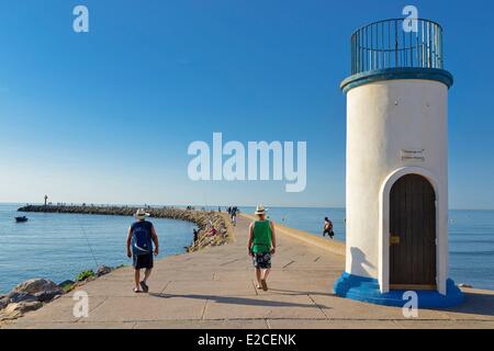 France, Herault, Valras Plage, small lighthouse on the pier in homage to the disappeared fishermen, combed mens of hats and it bernudas walking on a dike in front of the sea Stock Photo