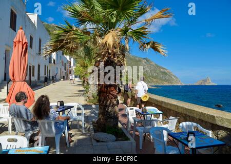 Italy, Sicily, Egadi islands, island of Marettimo, Via Campi, tourists seated at a cafe terrace under a palm tree in front sea Stock Photo