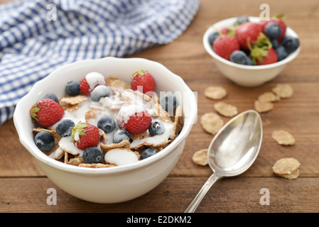 Whole-grain flakes with fresh berries in bowl and yogurt on wooden background Stock Photo