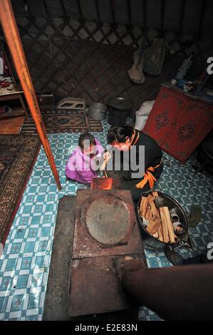 Mongolia, Tov province, Baganuur, father standing by daughter, holding log by fireplace in yurt Stock Photo