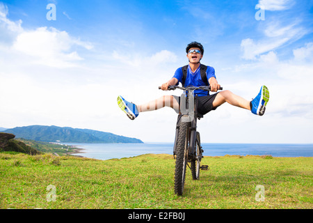 funny young backpacker riding a bicycle on a meadow Stock Photo