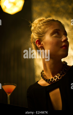 Woman sitting alone at night club bar looking away expectantly Stock Photo