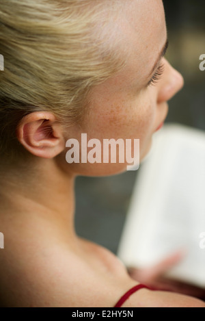 Woman looking away in thought while reading book, cropped Stock Photo