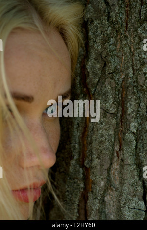 Young woman leaning against tree trunk, looking away sadly Stock Photo