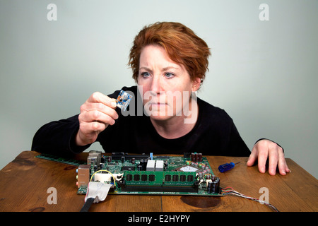 Female engineer examining computer chip removed from a laptop motherboard. Stock Photo
