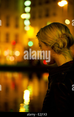 Young woman at night by river illuminated by city lights Stock Photo