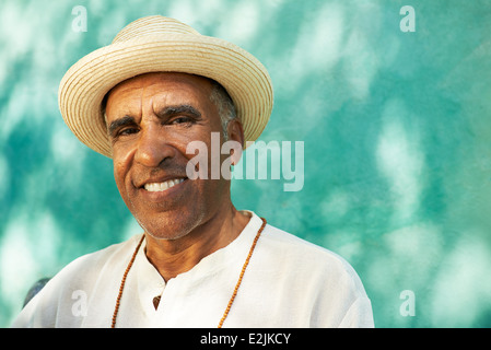 Portrait of retired senior hispanic man with straw hat sitting in park and looking at camera with happy expression Stock Photo