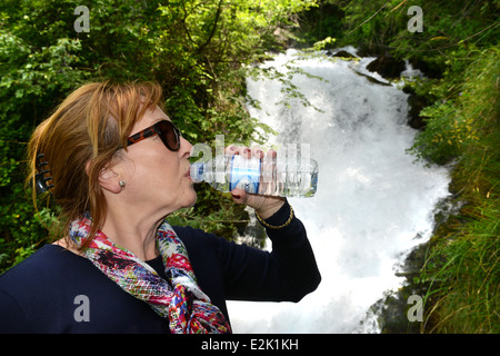 Woman drinking bottled natural water next to Fiumelatte river Varenna Lombardy Italy Stock Photo