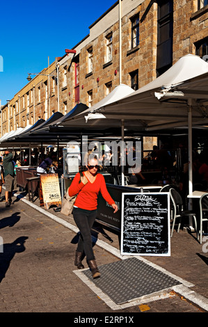 Hobart Australia / A young woman walks past diners in Salamanca Place, Hobart Tasmania Australia Stock Photo