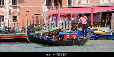 Close up view Venetian gondolier man working & standing using a mobile phone aboard his gondola at station on the Grand Canal Venice Veneto Italy Stock Photo