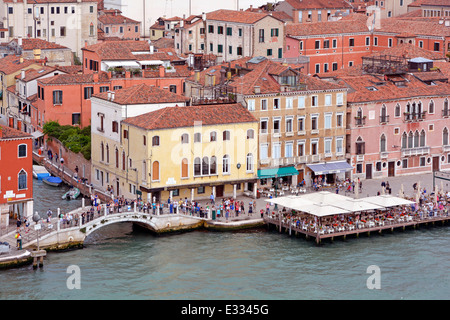 View from cruise ship departing Venice along Giudecca Canal passing Venetian canal footbridge & floating restaurant along Ponte Longo Veneto Italy Stock Photo