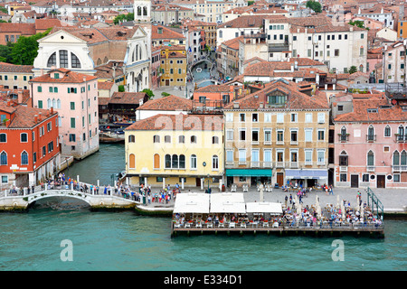 View from cruise ship departing Venice along Giudecca Canal passing Venetian canal footbridge & floating restaurant along Ponte Longo Veneto Italy Stock Photo