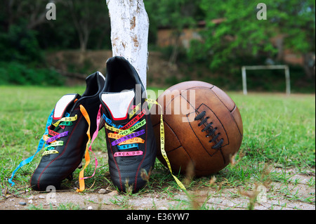 Good luck soccer football boots soccer cleats laced with Brazilian wish ribbons on rustic dirt grass pitch with vintage brown Stock Photo
