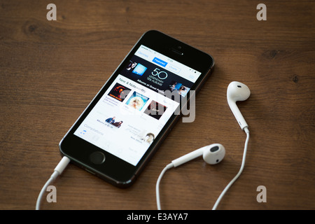 Brand new Apple iPhone 5S with iTunes store application on the screen lying on a desk with headphones Stock Photo