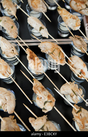 Closeup of rows of cooked chicken appetizers on wooden skewers resting on glasses with mayonnaise sauce dip ready for serving Stock Photo