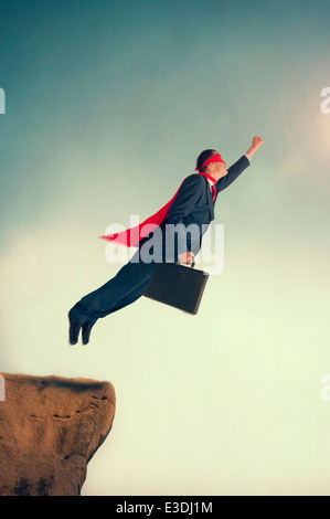 superhero businessman taking off to flight from a cliff ledge wearing a cape and mask Stock Photo
