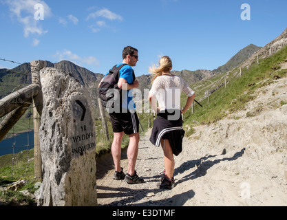 Ill-equipped walkers by direction sign on Pyg Track looking towards Mt Snowdon in mountains of Snowdonia North Wales UK Britain Stock Photo