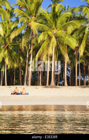 Two people sitting on beach under palm trees; Las Cabanos; El Nido; Bacuit Bay; Palawan; Philippines Stock Photo