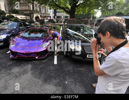 Passers-by stop to check out two flashy cars parked outside the front of The Dorchester Hotel. A purple Lamborghini Aventador and yellow and gold Bugatti Veyron.  Featuring: Lamborghini Aventador Where: London, United Kingdom When: 20 Oct 2013 Stock Photo