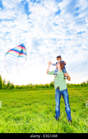 Smiling father holds kid and watches kite in air Stock Photo