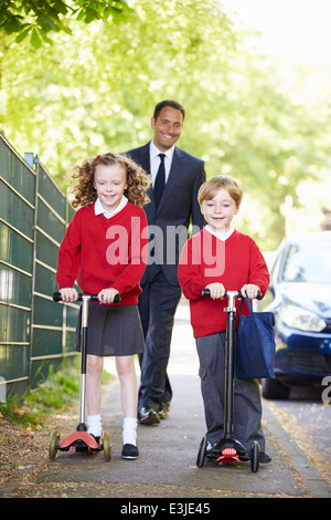 Children Riding Scooters On Their Way To School With Father Stock Photo