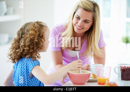 Mother And Daughter Having Breakfast In Kitchen Together Stock Photo