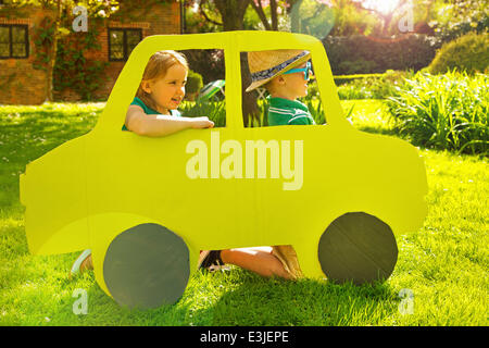 Boy and Girl Kneeling behind Cardboard Cut Out in Shape of Car