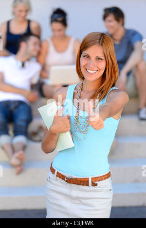 Smiling college student girl thumb-up friends in background summer time Stock Photo