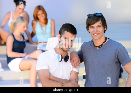 Two student boys standing outside college summer friends in background Stock Photo