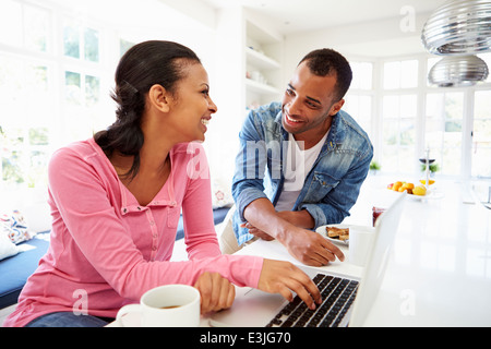 Couple Having Breakfast And Using Laptop In Kitchen Stock Photo
