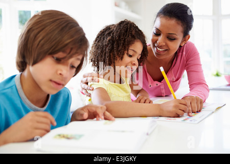 Mother Helping Children With Homework In Kitchen Stock Photo