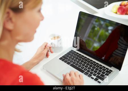 Woman Using Laptop At Home In Kitchen Stock Photo