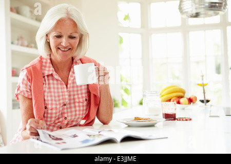 Middle Aged Woman Reading Magazine Over Breakfast Stock Photo