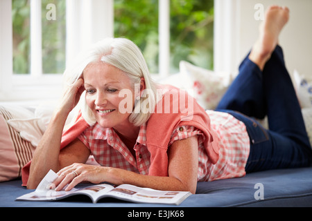 Middle Aged Woman Reading Magazine Lying On Sofa Stock Photo
