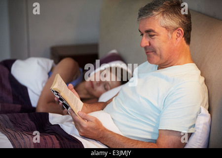 Middle Aged Couple In Bed Together With Man Reading Book Stock Photo