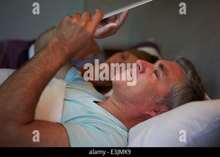 Middle Aged Couple In Bed With Man Using Tablet Computer Stock Photo