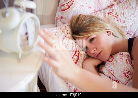 Teenage Girl Waking Up In Bed And Turning Off Alarm Clock Stock Photo