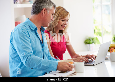 Couple Using Laptop Whilst Having Breakfast In Kitchen Stock Photo