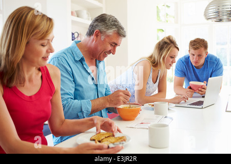 Teenage Family Having Breakfast In Kitchen With Laptop Stock Photo