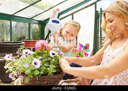 Mother And Daughter Watering Plants In Greenhouse Stock Photo