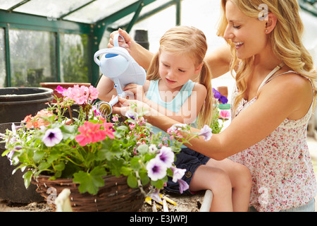 Mother And Daughter Watering Plants In Greenhouse Stock Photo