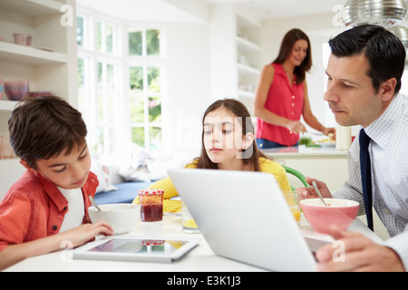 Family Using Digital Devices At Breakfast Table Stock Photo