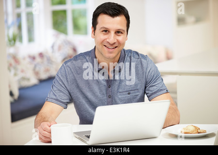 Hispanic Man Using Laptop In Kitchen At Home Stock Photo