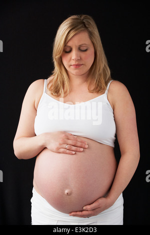 Portrait Of Pregnant Woman Wearing White On Black Background Stock Photo