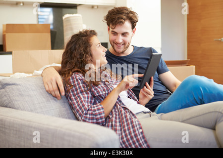Couple Relaxing On Sofa With Digital Tablet In New Home Stock Photo