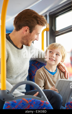 Son Using Digital Tablet On Bus Journey With Father Stock Photo