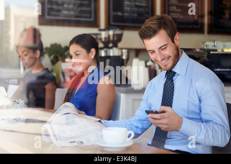 Businessman With Mobile Phone And Newspaper In Coffee Shop Stock Photo