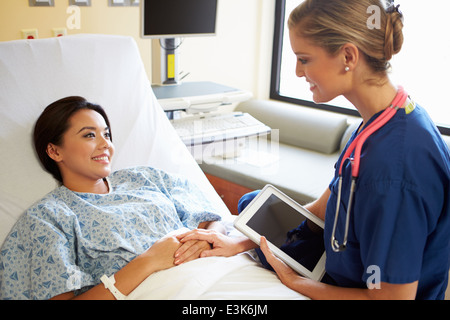 Nurse Talking To Female Patient On Ward Using Digital Tablet Stock Photo