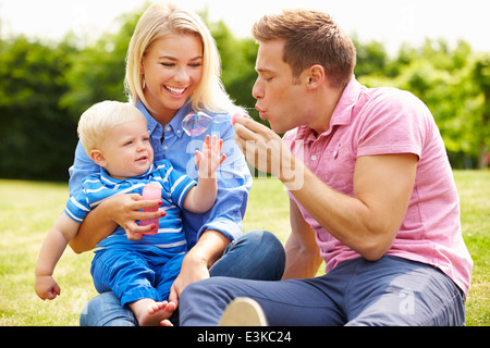 Parents Blowing Bubbles For Young Boy In Garden Stock Photo